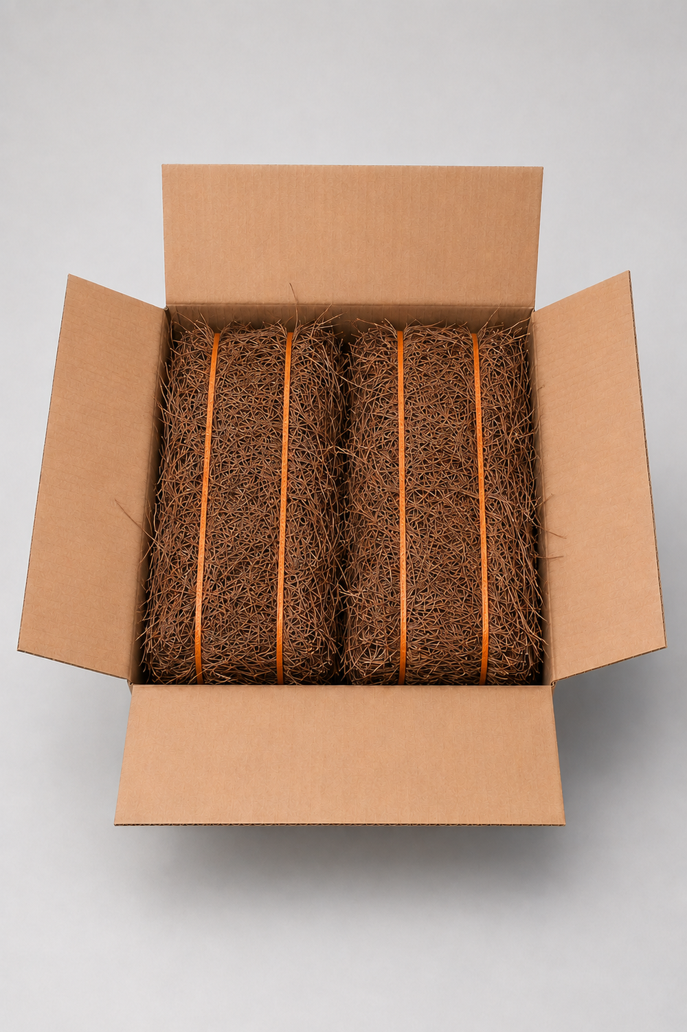 An open brown cardboard box viewed from above, containing two bundled strips of natural coir rope secured with orange bands, on a light gray background.